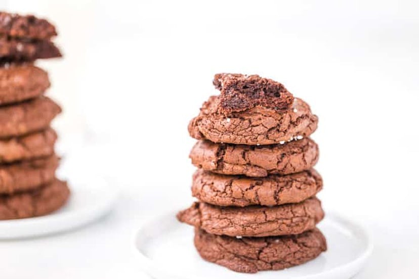 chocolate brownie cookies stacked on a white plate, with bites taken out of the top cookie
