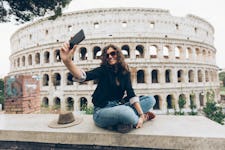 Young traveler with travel bio on her Instagram, taking a selfie in front of the Colosseum in Rome.