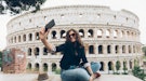 Young traveler with travel bio on her Instagram, taking a selfie in front of the Colosseum in Rome.