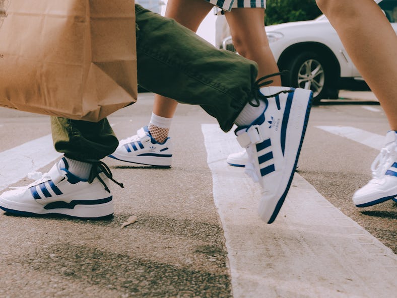 A group of women walking across the street, all of them wearing blue and white Adidas Forum Low snea...