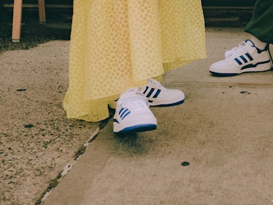 An anonymous woman in a yellow maxi dress with blue and white Adidas Forum sneakers on underneath