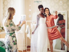 Young bride trying out her wedding dress, taking a selfie with her friend before posting on Instagra...