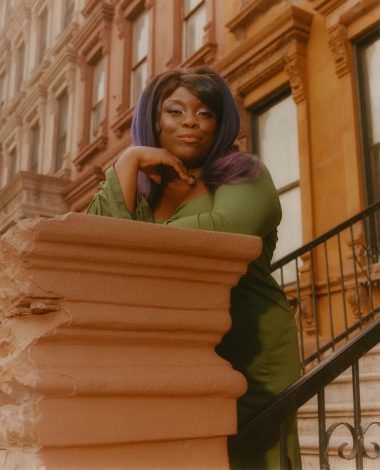 Yola stands on a stoop in a green dress