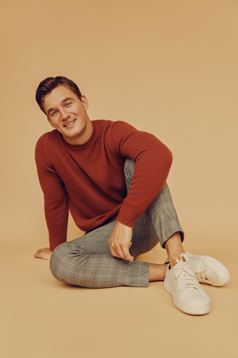 Tyler sitting and smiling in grey pants, white shoes and a red sweater
