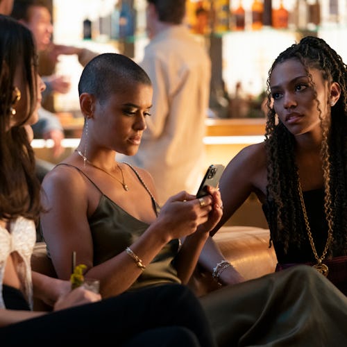 Characters from the Gossip Girl reboot sit on a couch at a club. Of the three girls, Julien, a Black...
