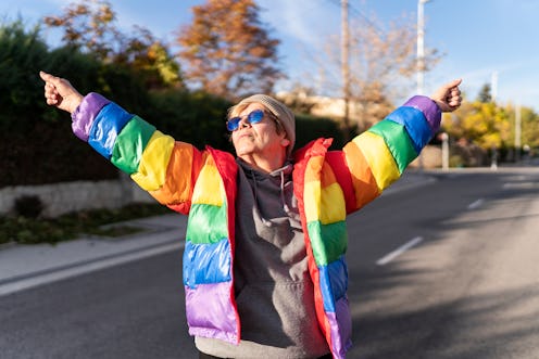 Woman in rainbow coat posing in the middle of the street.