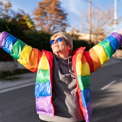 Woman in rainbow coat posing in the middle of the street.