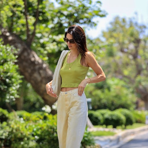 Kendall Jenner wears a green crop top, white jeans, and cowboy boots.