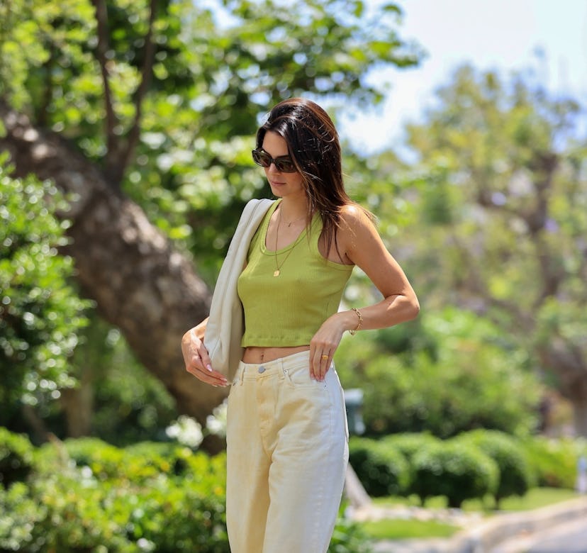 Kendall Jenner wears a green crop top, white jeans, and cowboy boots.