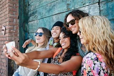 A group of friends smiling and taking a selfie at their high school reunion to post on Instagram wit...