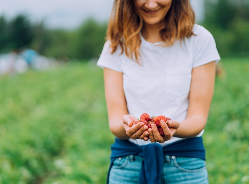 Young woman holding strawberries in a field before posting on Instagram with strawberry quotes, stra...