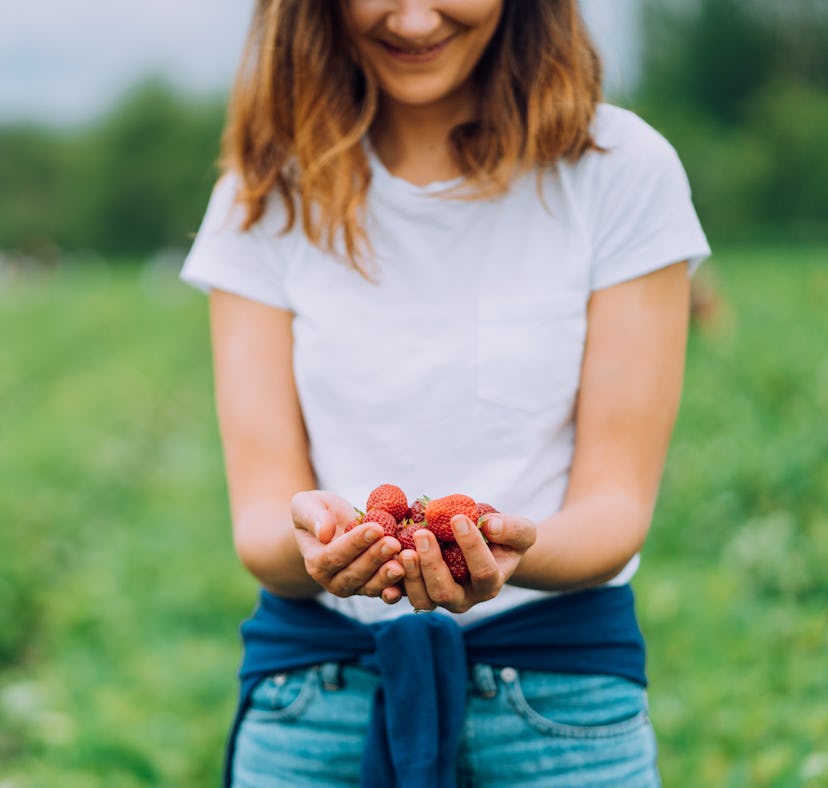 Young woman holding strawberries in a field before posting on Instagram with strawberry quotes, stra...
