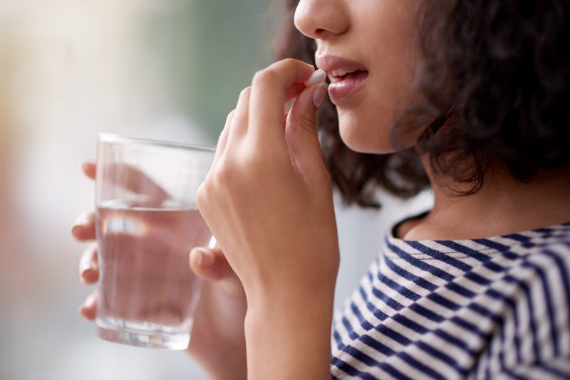 Woman taking a pill with a glass of water.