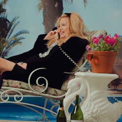 Jennifer Coolidge laughing during a phone call with a glass of champagne