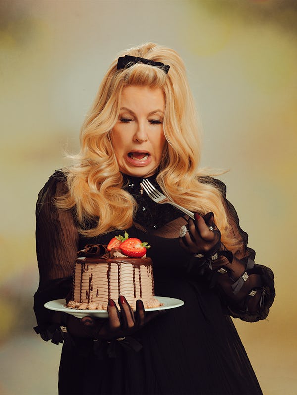 Jennifer Coolidge in a black Gucci dress and gloves, holding a chocolate strawberry cake and fork 