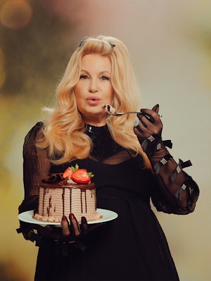 Jennifer Coolidge in a black Gucci dress and gloves, holding a chocolate strawberry cake and fork 