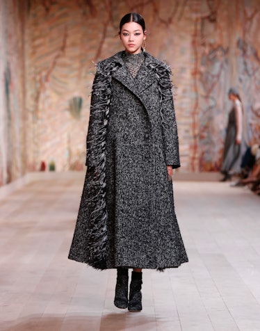 A model walking the runway in a grey Dior coat with a matching scarf 