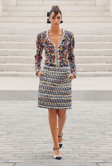 A model walking in a Chanel floral blouse and skirt with white and black shoes 