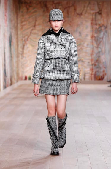 A model walking the runway in a houndstooth grey skirt and jacket with a matching cap by Dior Haute ...