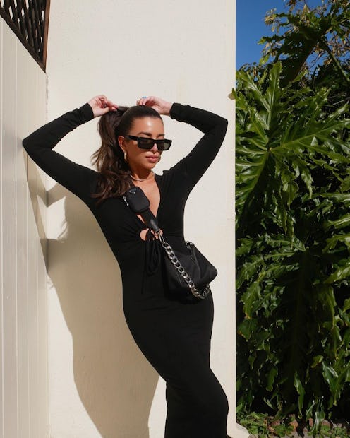 Melany C. Rodriguez in a black dress and sunglasses adjust her chic hair updo