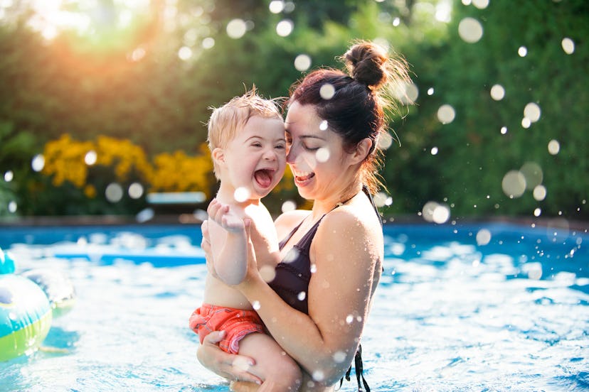 woman holding toddler son in pool with splashes of water
