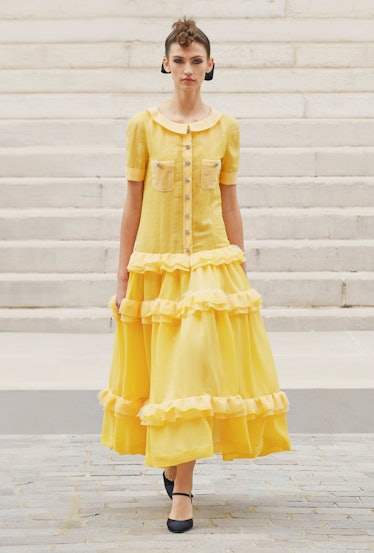 A model walking in a yellow, short-sleeved Chanel gown with ruffles 