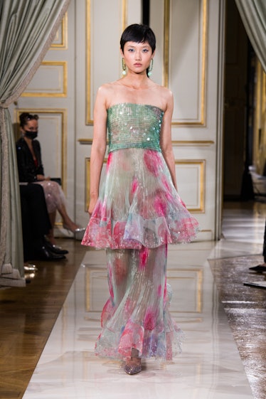 A model walking the runway in a sheer gown with a sparkly green top and white with touches of red on...