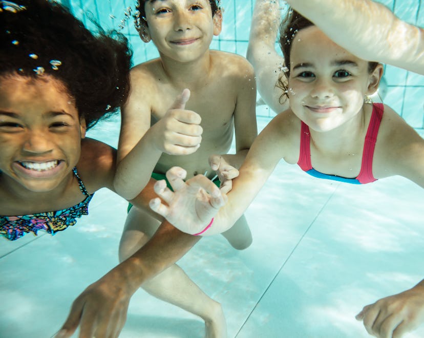 Kids swimming underwater, smiling at camera