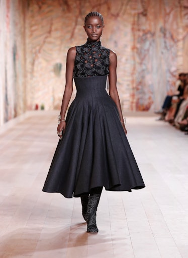 A model walking the runway in a black Dior, angle-length gown 