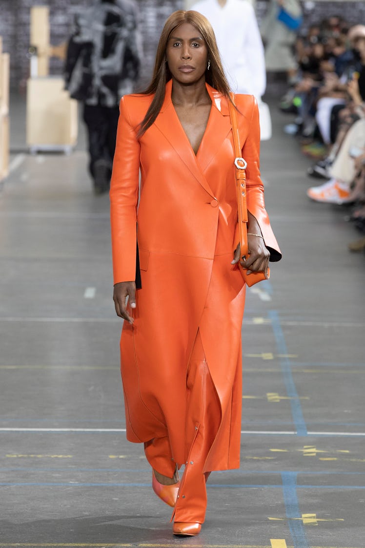 A model walking the runway for Off-White Fall 2021 in a long orange leather coat, matching pants and...