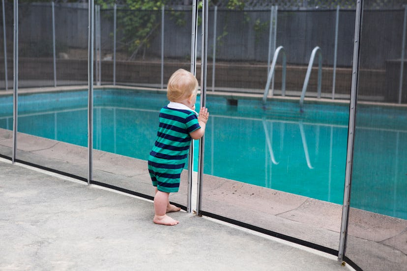 Baby standing in front of gate separating him from a pool