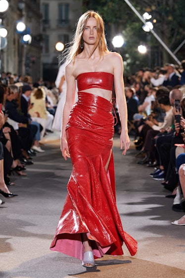 A model in a red shimmery leather gown with a slit down the side Alaïa 