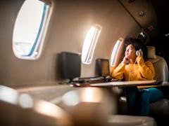 Young woman sitting on an airplane with headphones on, looking out the window before posting a pic o...