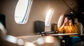 Young woman sitting on an airplane with headphones on, looking out the window before posting a pic o...