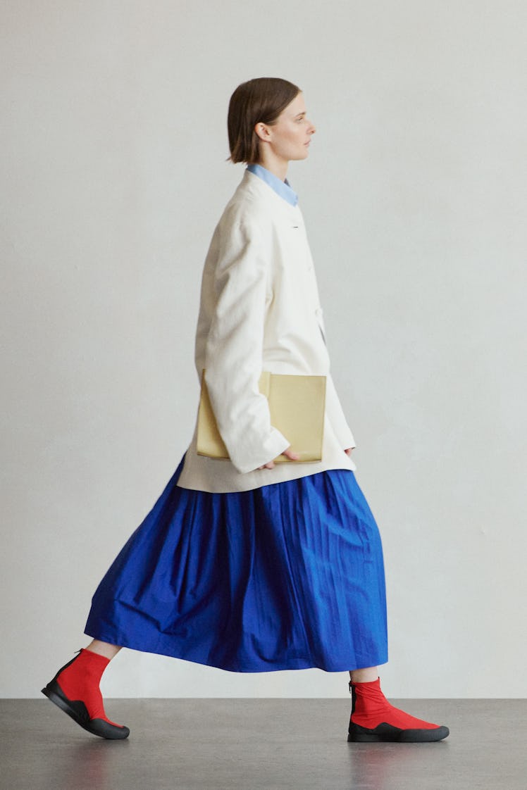 A female model walking while wearing a white blazer and a blue dress