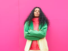 Young Cancer woman looking at the camera with a bright pink background.