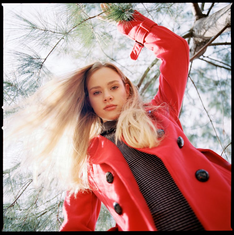 Young woman in a red coat staring down at the camera as one of the most manipulative zodiac signs.