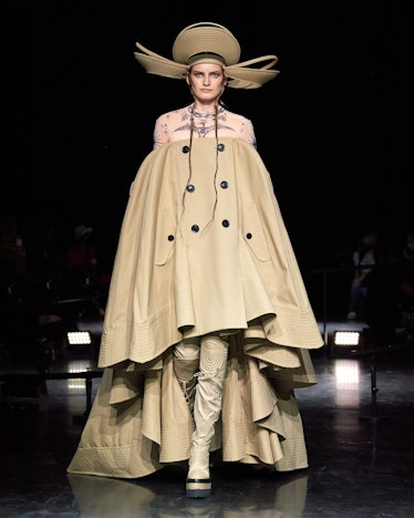 A model walking the Jean Paul Gaultier runway in an oversized beige gown with buttons down the middl...