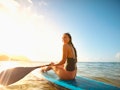 Young woman on a paddleboard in Hawaii, ready to take a pic for Instagram with a tropical caption.