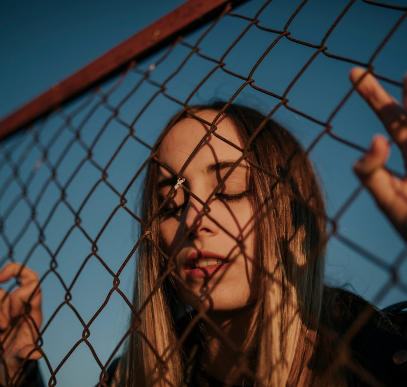 Young woman holding on to gate on Friday the 13th 2021, having the the worst day, per her zodiac sig...
