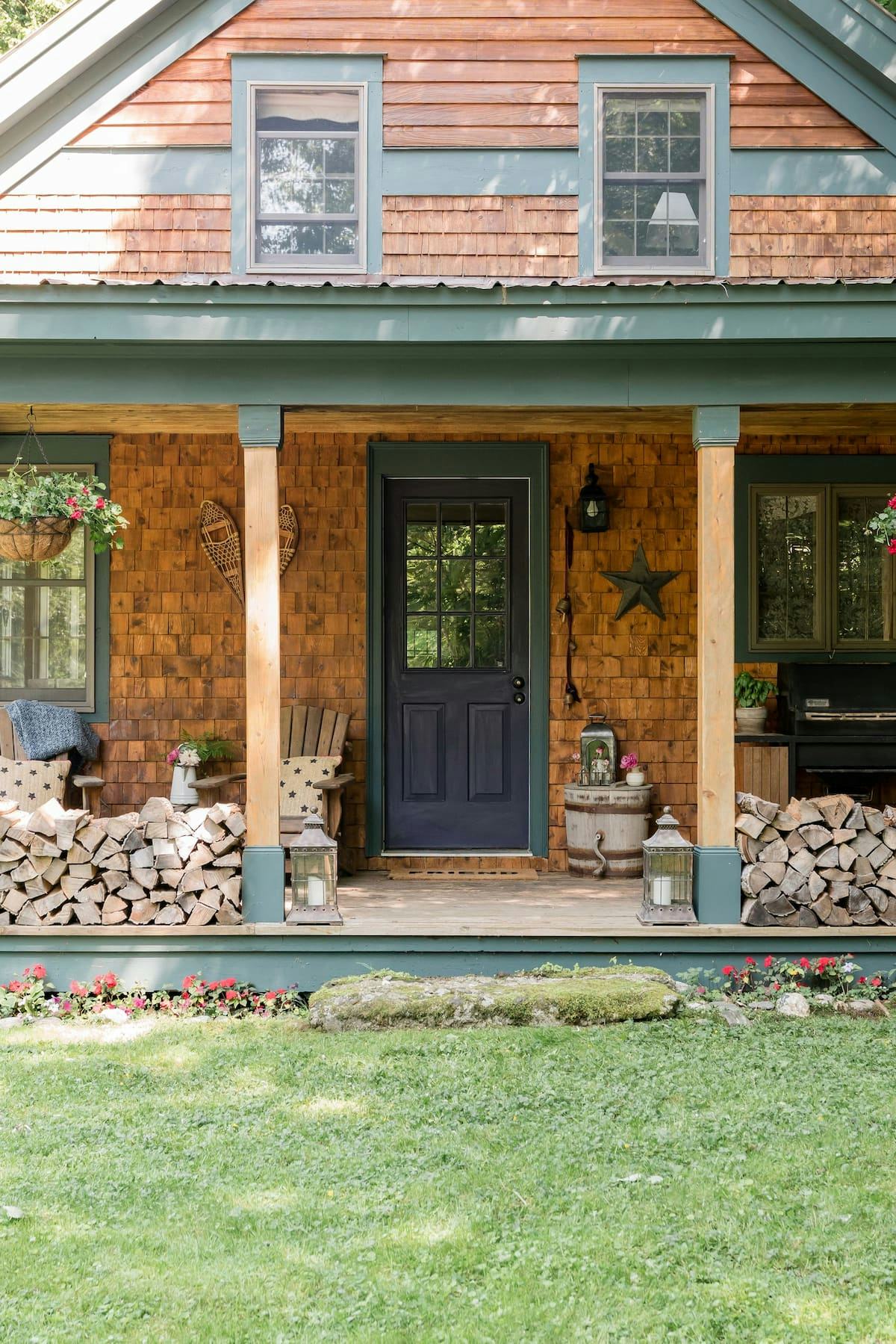 A cozy cabin with a wood tile wall, a black door and firewood stacked in the front 