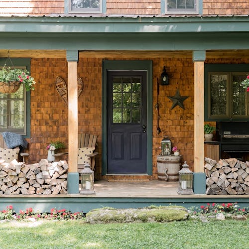 A cozy cabin with a wood tile wall, a black door and firewood stacked in the front 