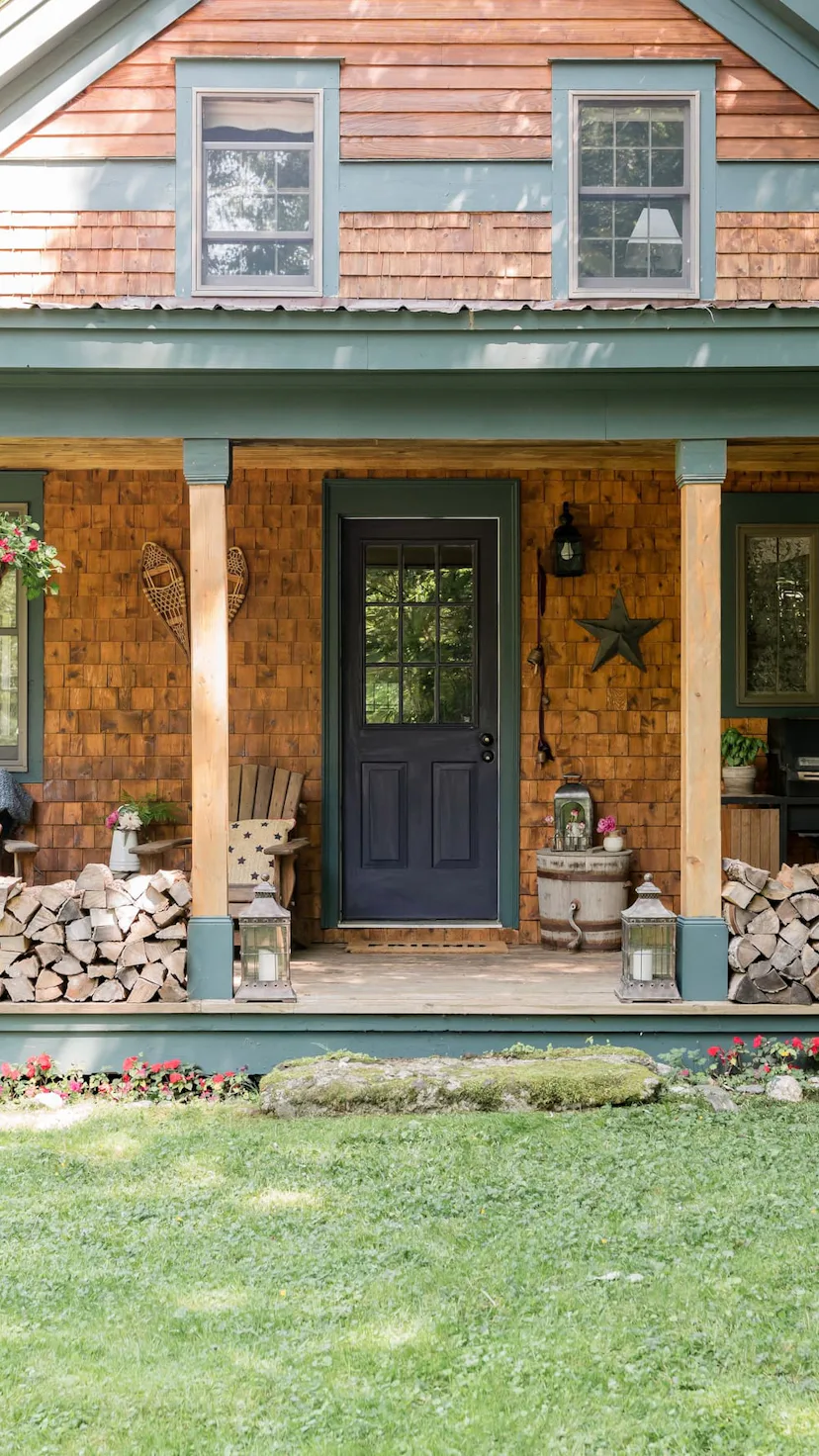 A cozy cabin with a wood tile wall, a black door and firewood stacked in the front