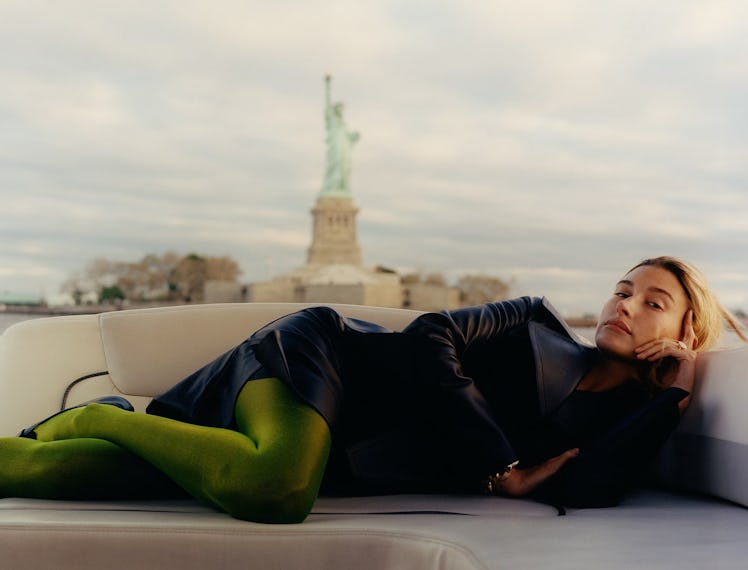 Hailey Bieber lying in a black dress with the Statue of Liberty behind her