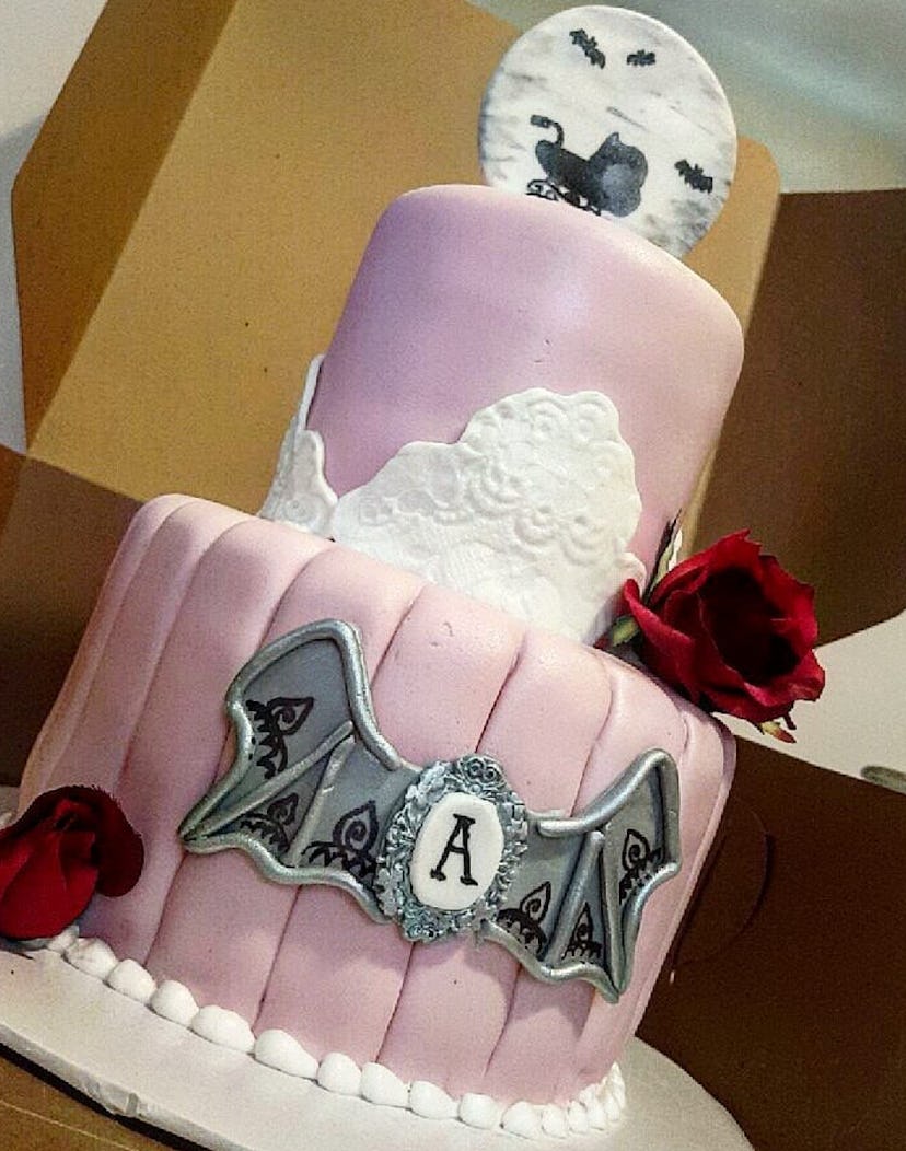 Two tiered pink cake with a silver bat, and a spooky topper with a moon, bats, and baby carriage