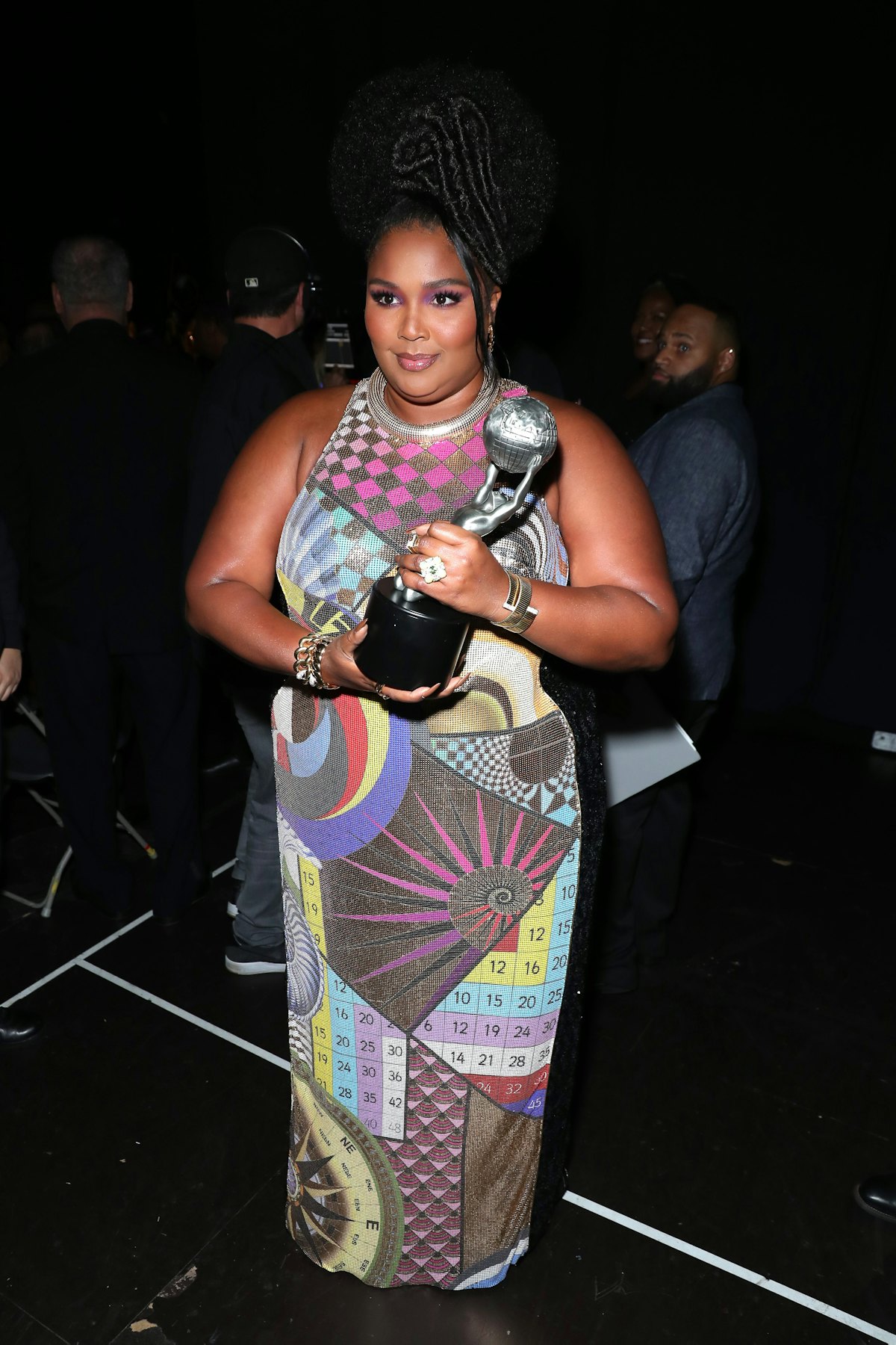 Lizzo in a mutlicolored dress with a trophy. 