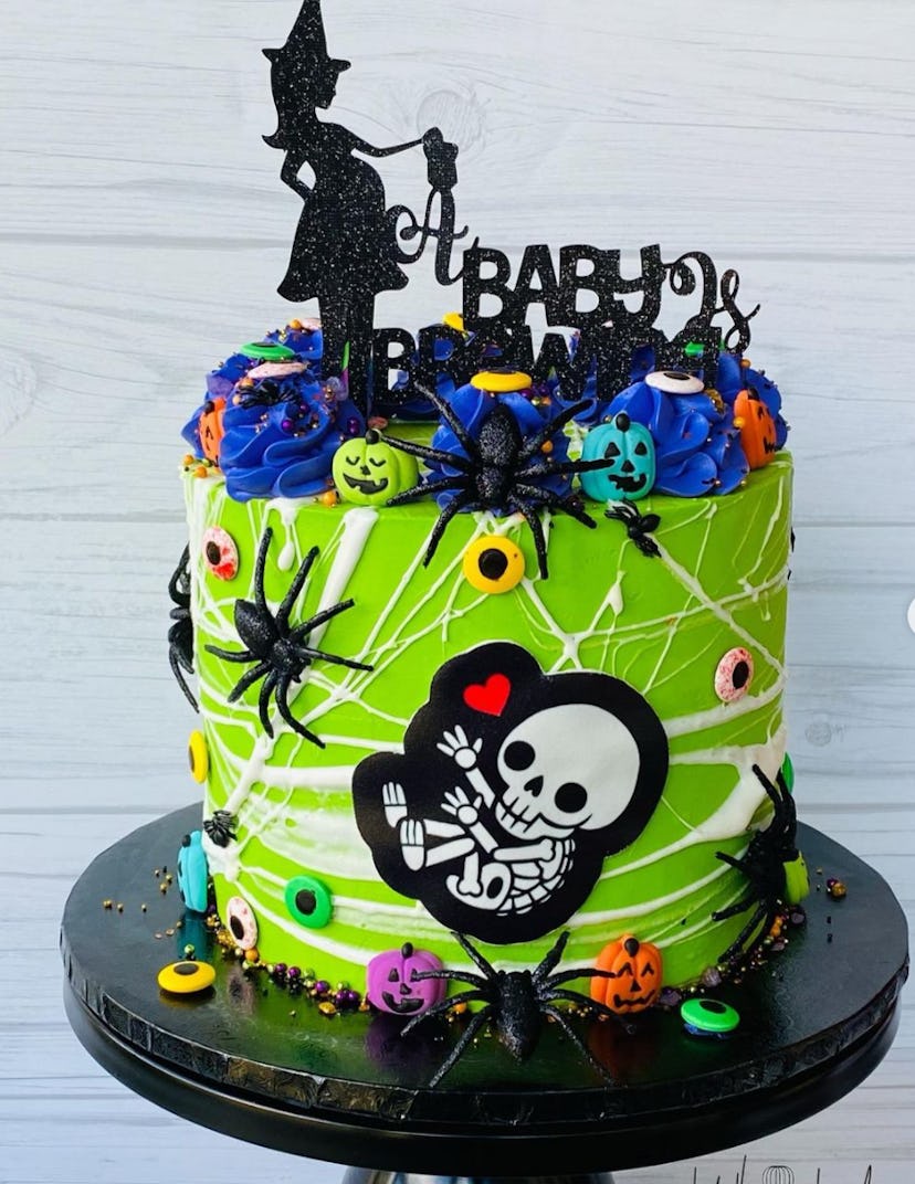 Green cake with Halloween details, spider webs, and a pregnant witch cake topper