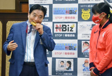 Nagoya mayor Takashi Kawamura bites into an Olympic gold medal belonging to softball player Miu Goto...