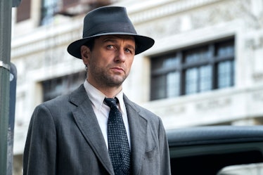 Matthew Rhys as Perry Mason in a grey trench coat and grey hat, with a white button-up and tie