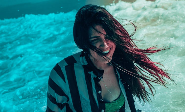 Young woman smiling while standing in the ocean, having the best week of August 16, 2021, per her zo...